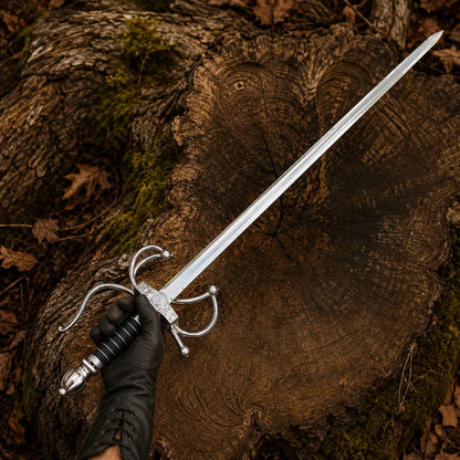 Gloved hand presenting the El Cid Rapier Sword with polished silver blade and decorative swept-hilt guard in a woodland setting