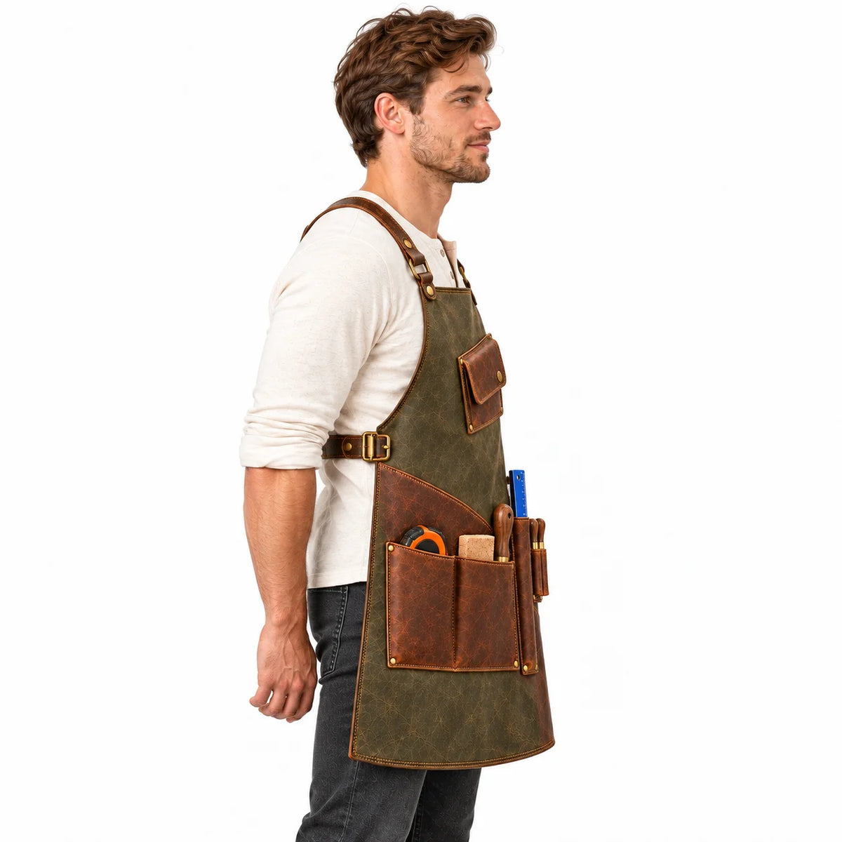 Side profile of male model wearing an olive leather workshop apron with brown utility pockets, side buckle and shoulder straps.