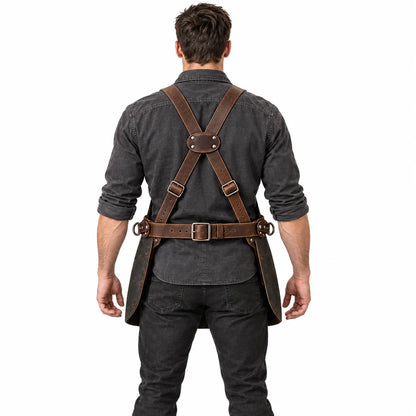 Rear view of male model demonstrating the brown cross-back harness and buckled waist fastening of a charcoal woodworking apron.