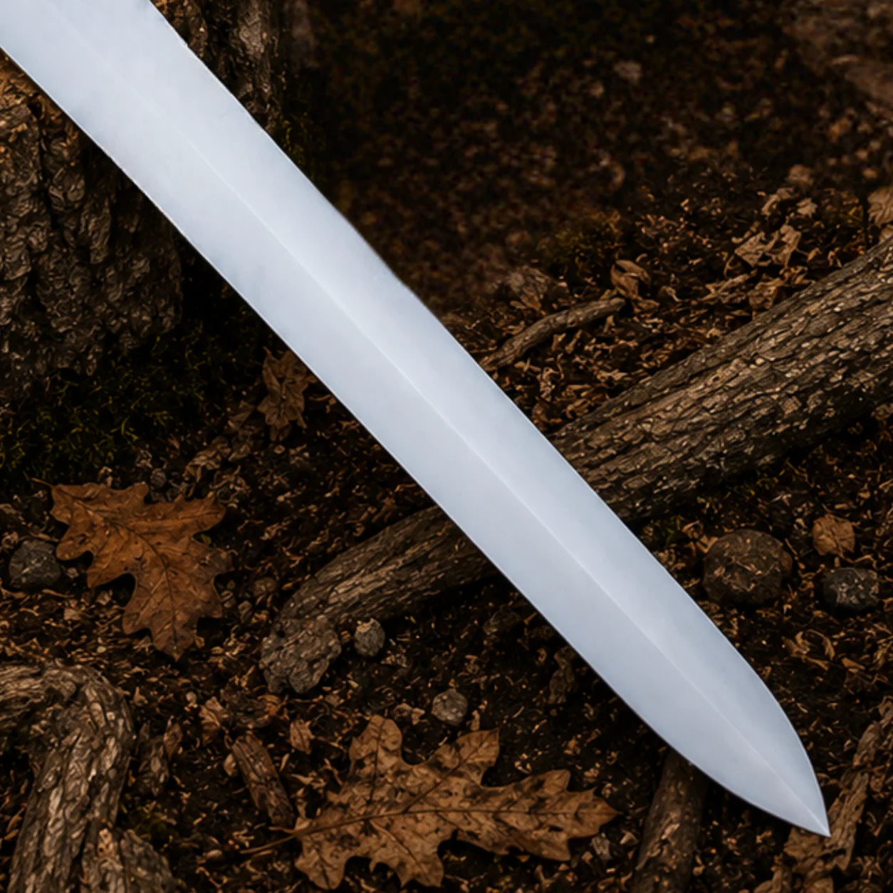 Detailed close-up of the satin-finish stainless steel Power Sword blade and tapered point over a woodland floor