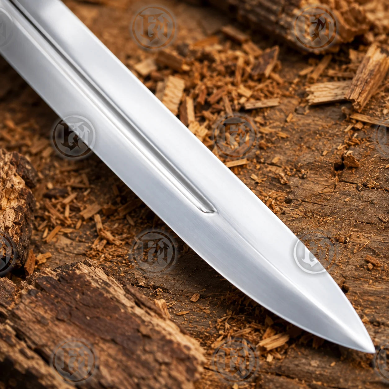Close-up of polished stainless-steel Power Sword blade tip showing the long central fuller against rustic timber