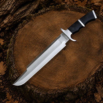 Full-length Predator Dutch Schaefer movie prop collectible with polished stainless steel section and ergonomic black handle on a tree stump